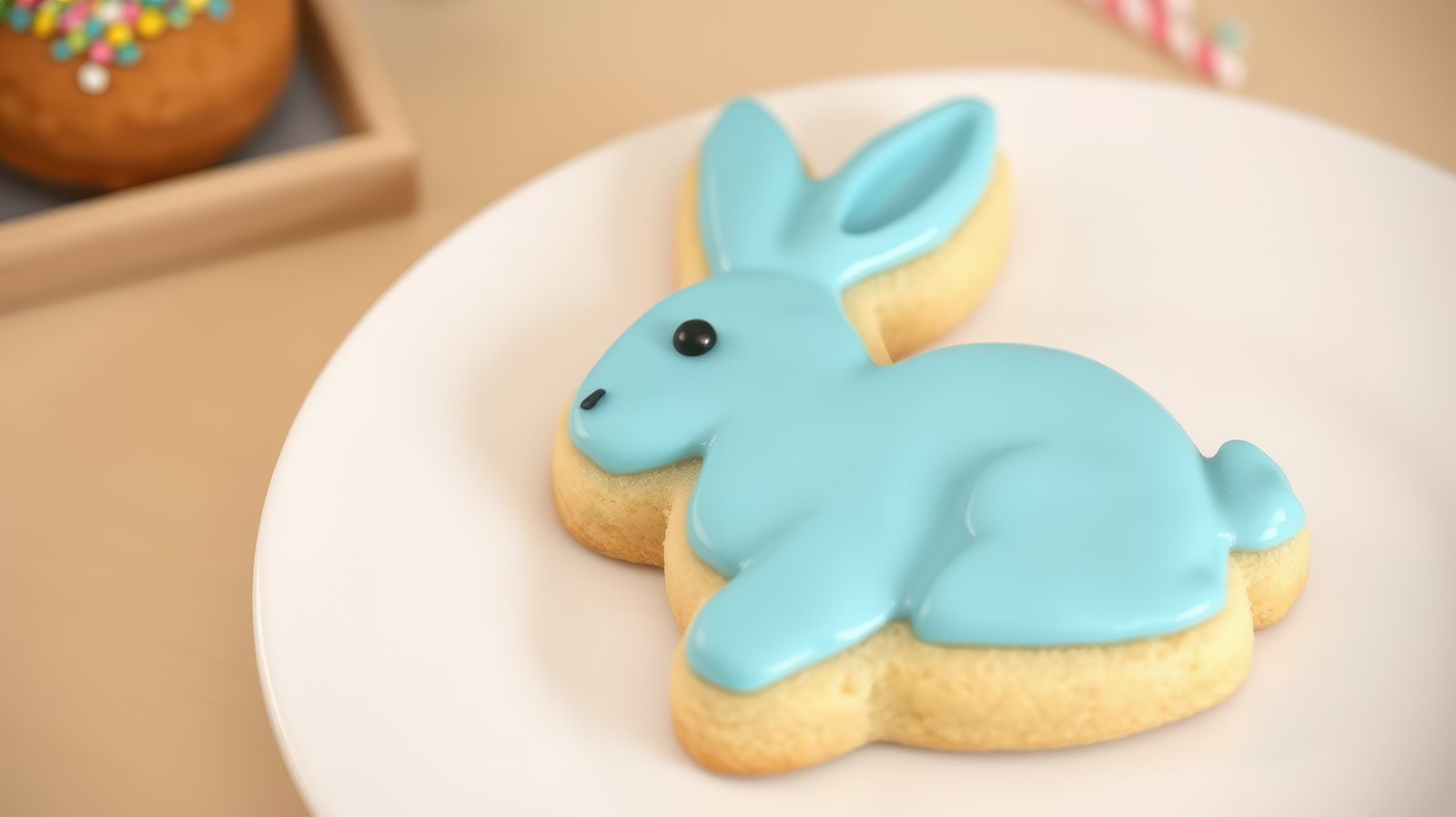 Colorful bunny-shaped cookie decorated with icing on a white plate surrounded by festive treats